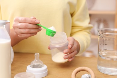 Photo of Woman preparing infant formula at table indoors, closeup. Baby milk