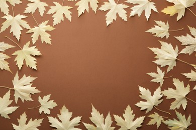 Photo of Frame of dry autumn leaves on brown background, flat lay. Space for text