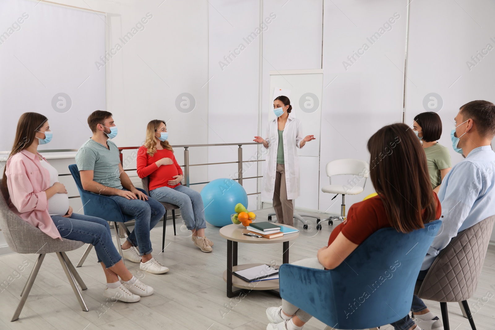 Photo of Group of pregnant women, men and doctor with protective masks at courses for expectant parents indoors