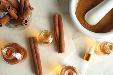 Photo of Bottles with essential oil and cinnamon sticks on marble table, flat lay