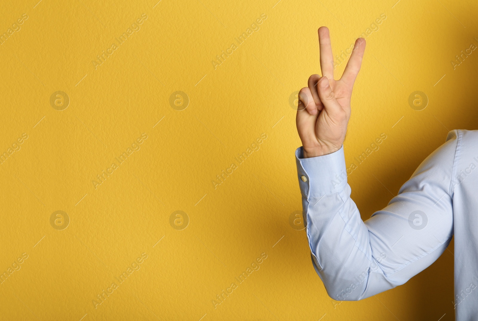 Photo of Young man showing victory gesture on color background. Space for text