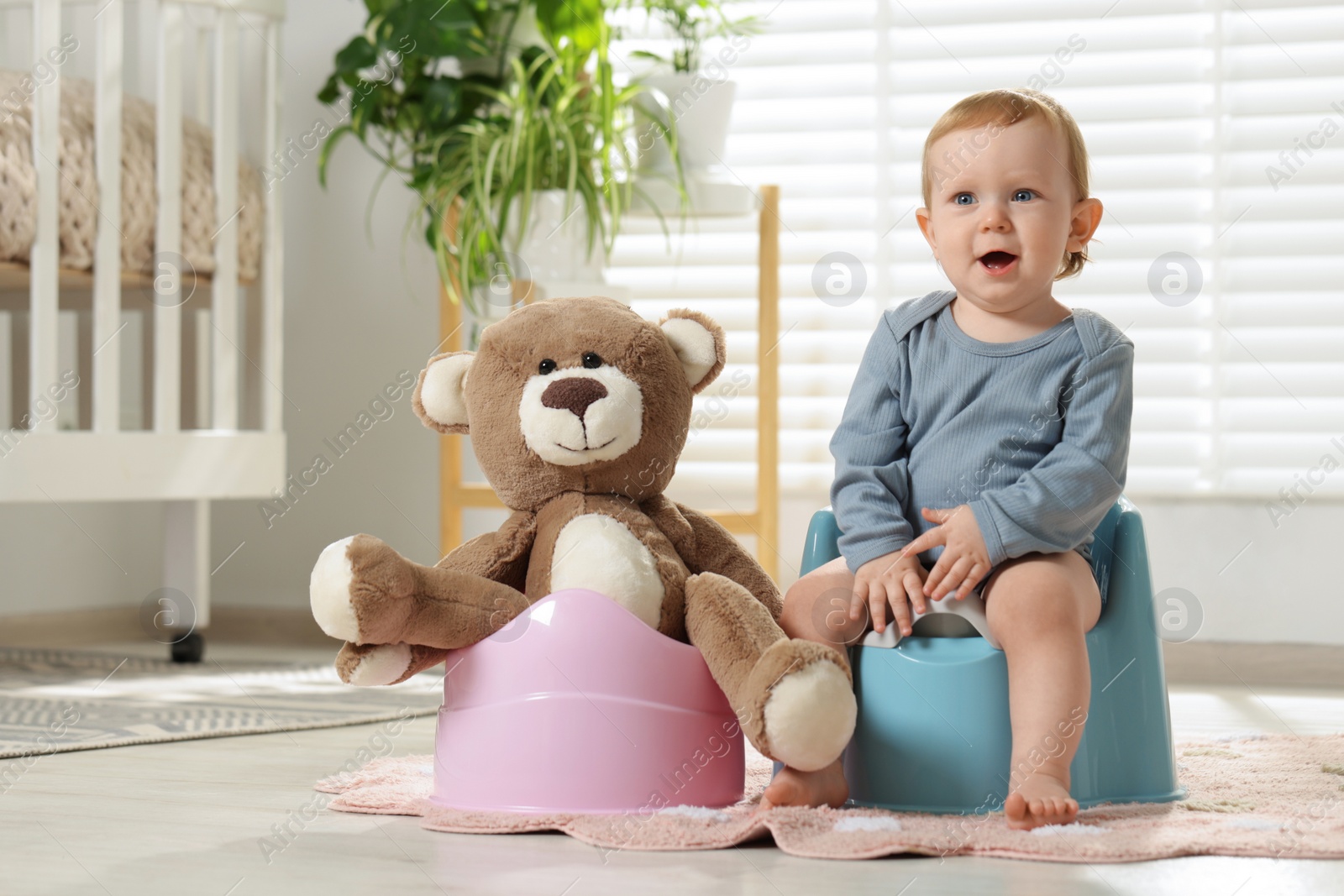 Photo of Little child and teddy bear sitting on plastic baby potties indoors