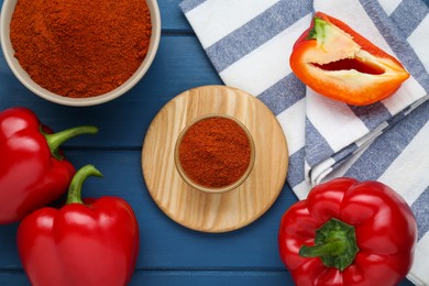 Photo of Bowls with aromatic paprika powder and fresh bell peppers on blue wooden table, flat lay