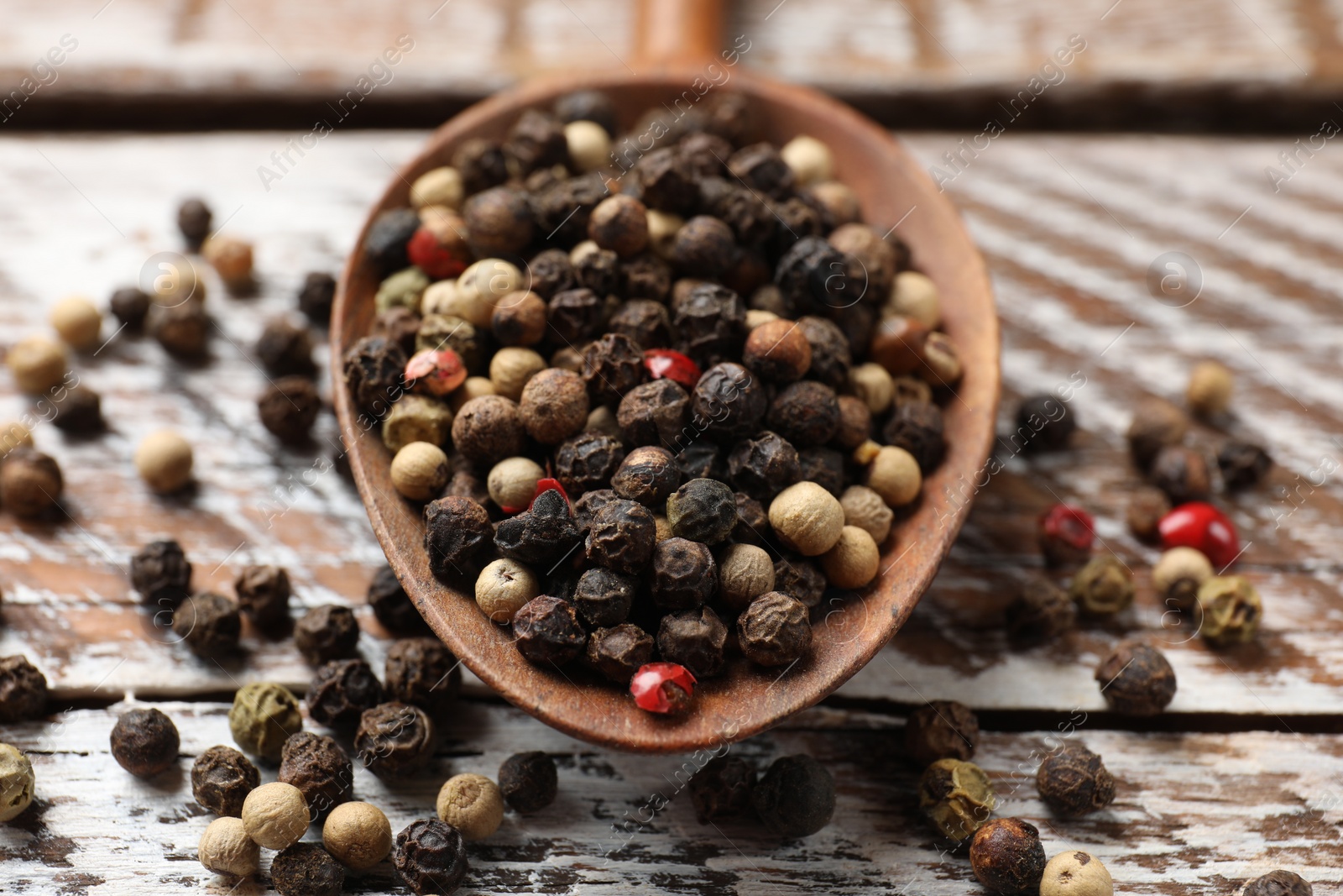 Photo of Aromatic spice. Different peppers in spoon on wooden table, closeup