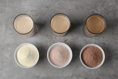 Glasses with protein shakes and powders in bowls on table, top view