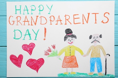 Photo of Beautiful drawing with phrase Happy Grandparents Day on blue wooden table, top view