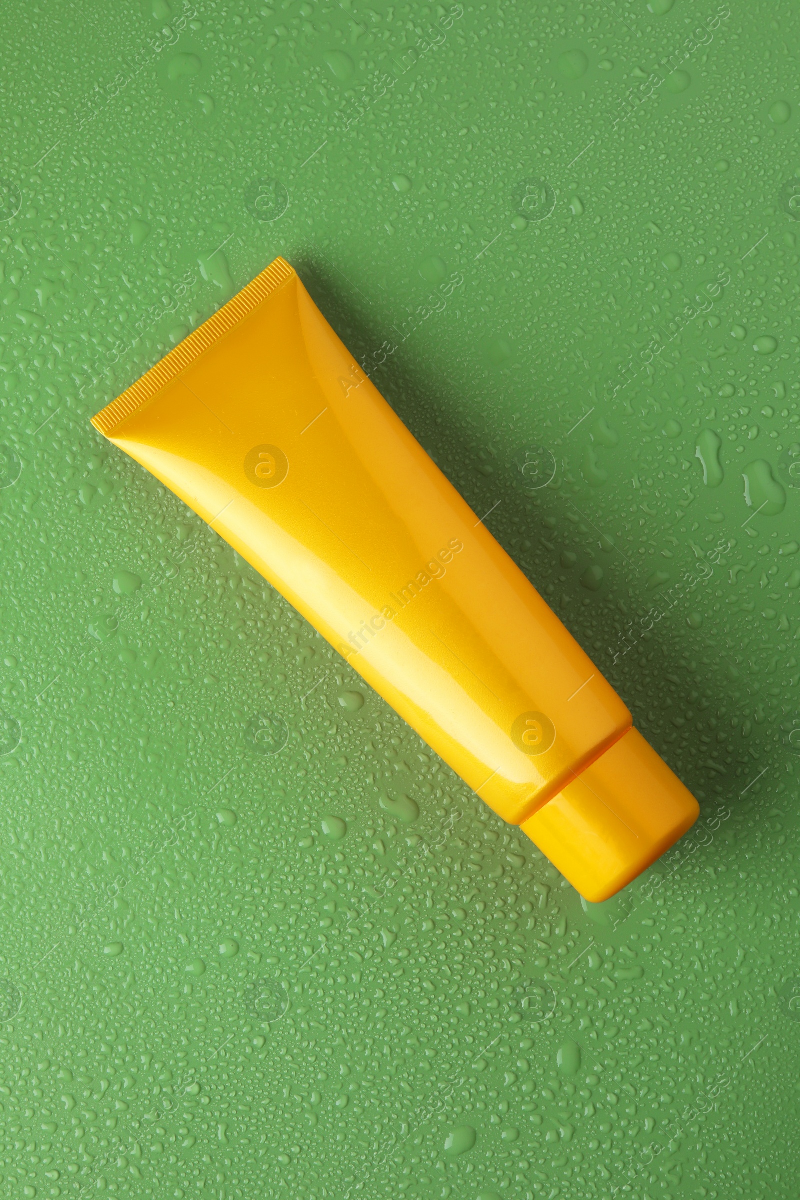 Photo of Moisturizing cream in tube on green background with water drops, top view