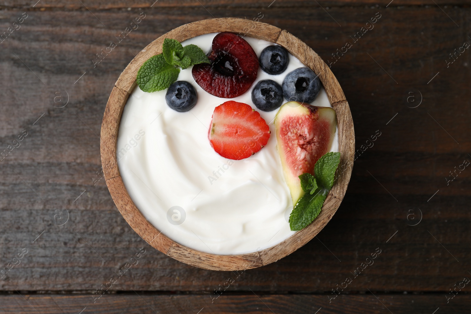 Photo of Bowl with yogurt, berries, fruits and mint on wooden table, top view