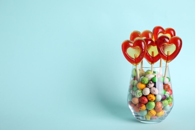 Photo of Delicious heart shaped lollipops and dragees in glass on turquoise background. Space for text