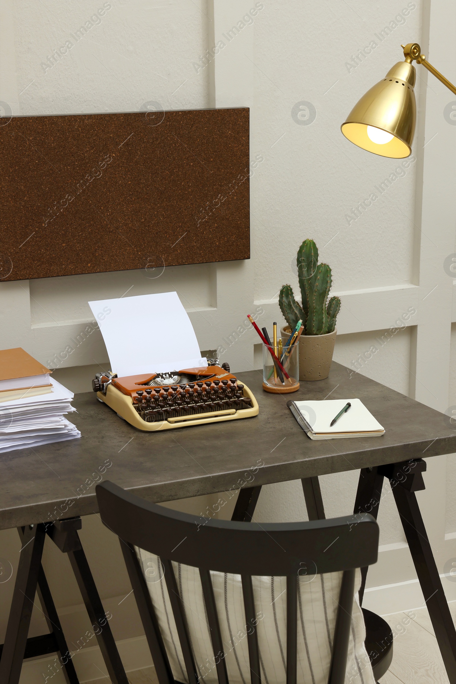 Photo of Typewriter and stack of papers on dark table in room. Writer's workplace