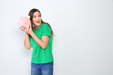 Young woman with piggy bank on white background. Space for text