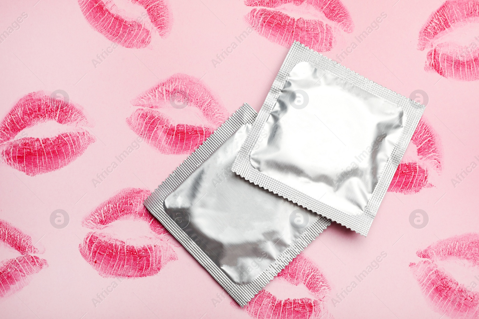 Photo of Condoms with lipstick kiss marks on pink background, flat lay. Safe sex