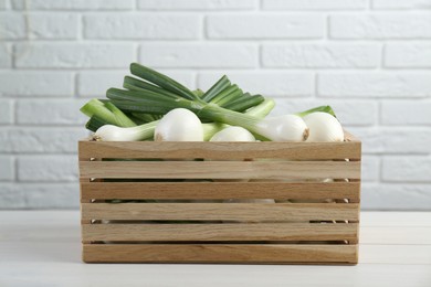 Photo of Crate with green spring onions on white wooden table