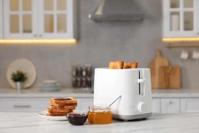 Photo of Making toasts for breakfast. Appliance, crunchy bread, honey and jam on white table in kitchen