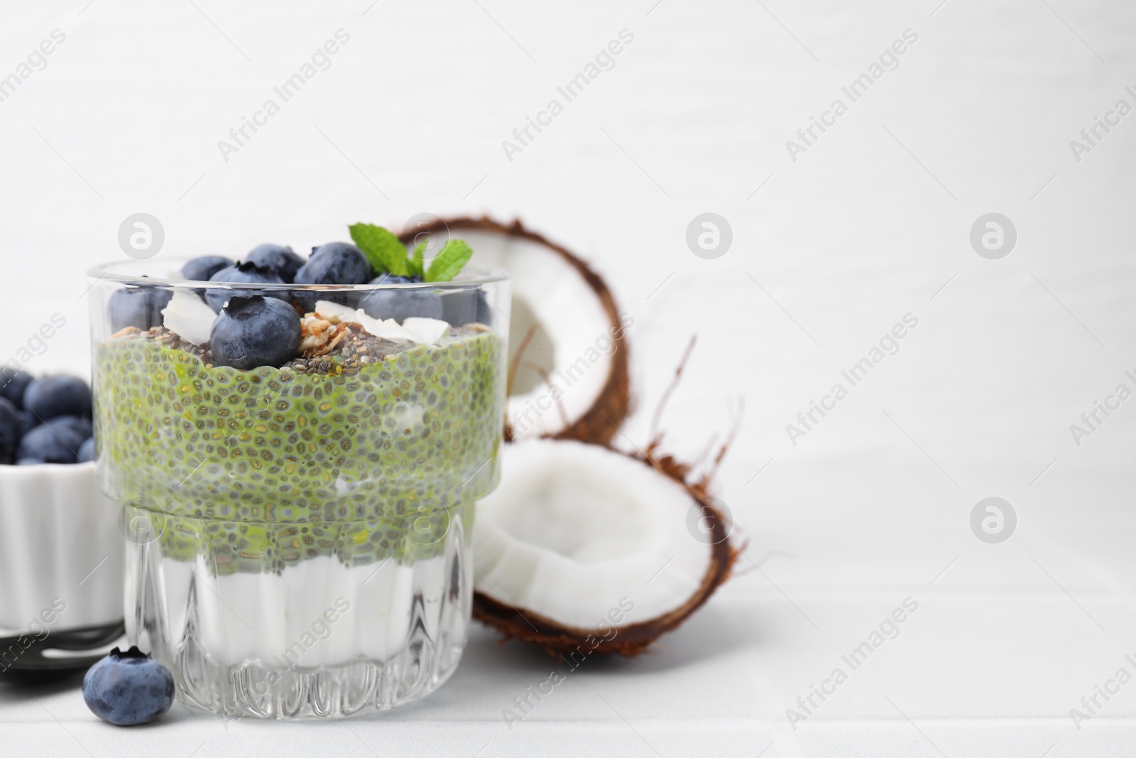 Photo of Tasty chia matcha pudding with coconut and blueberries on white table, space for text. Healthy breakfast