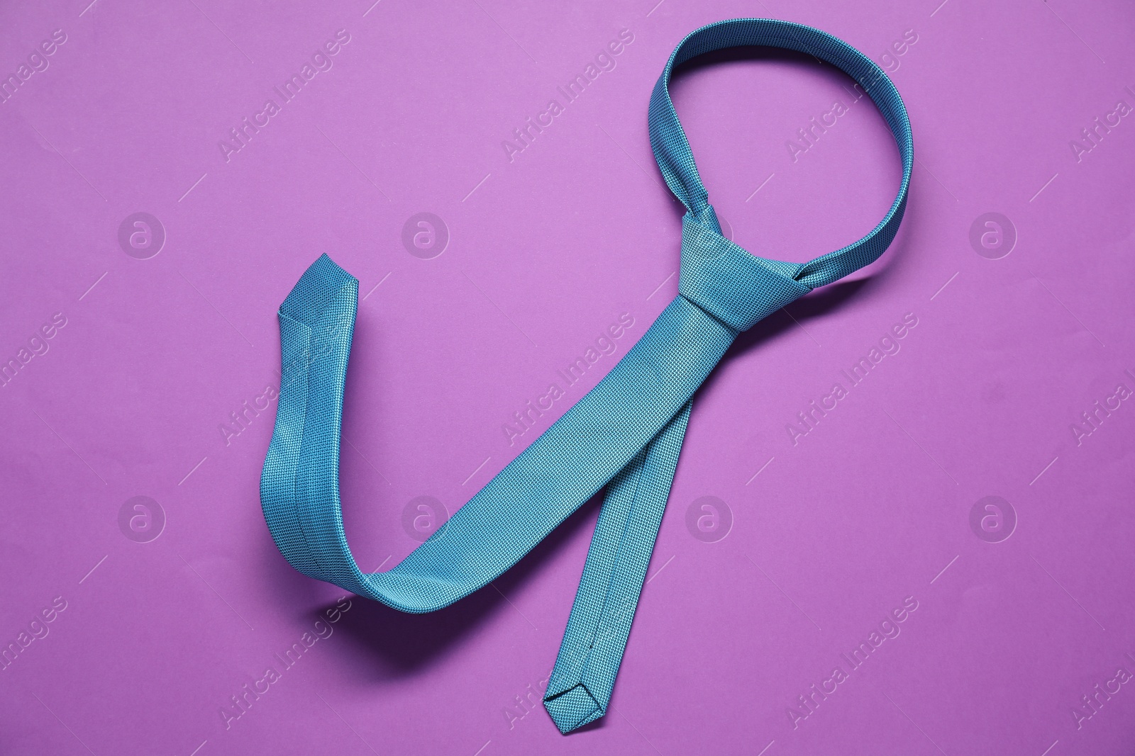 Photo of Turquoise necktie on purple background, top view