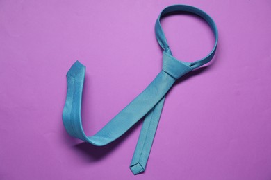 Turquoise necktie on purple background, top view