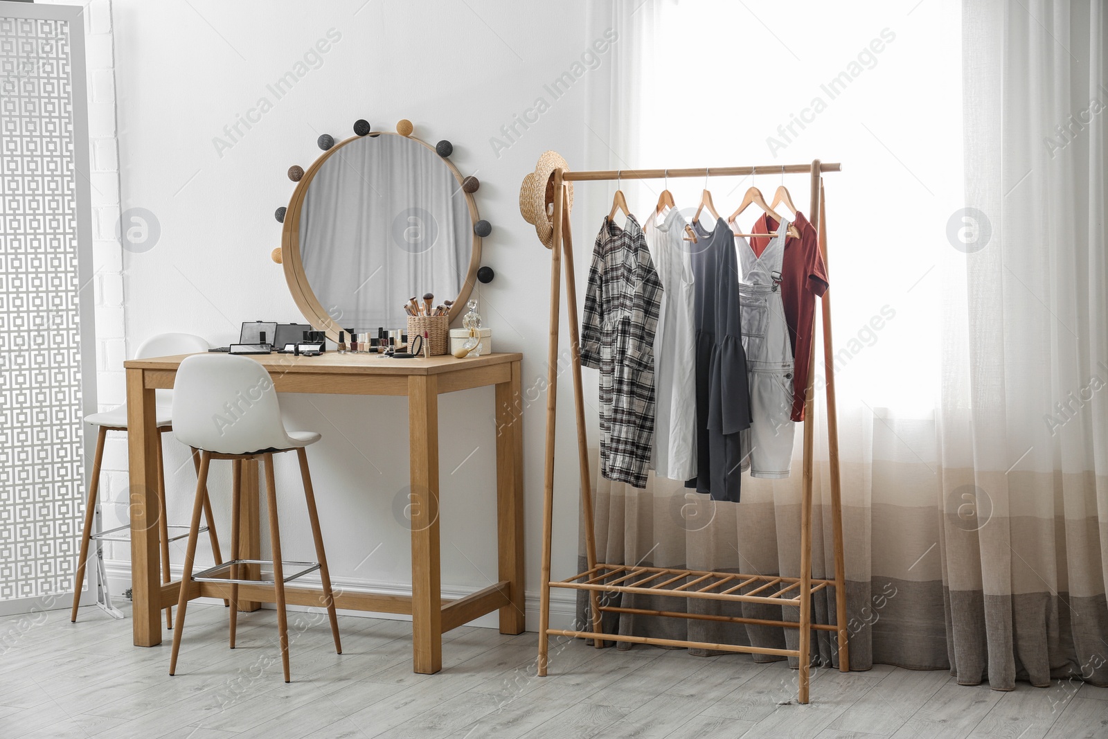 Photo of Hangers with stylish clothes on rack and dressing table in makeup room