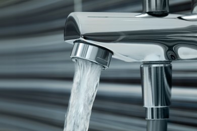 Photo of Water flowing from bath tap on blurred background, closeup