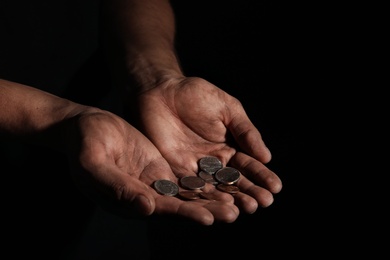 Photo of Poor man with coins on dark background, closeup
