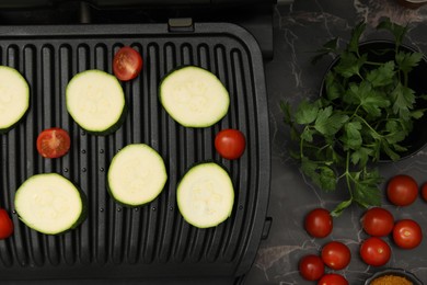 Photo of Electric grill with vegetables on black marble table, flat lay