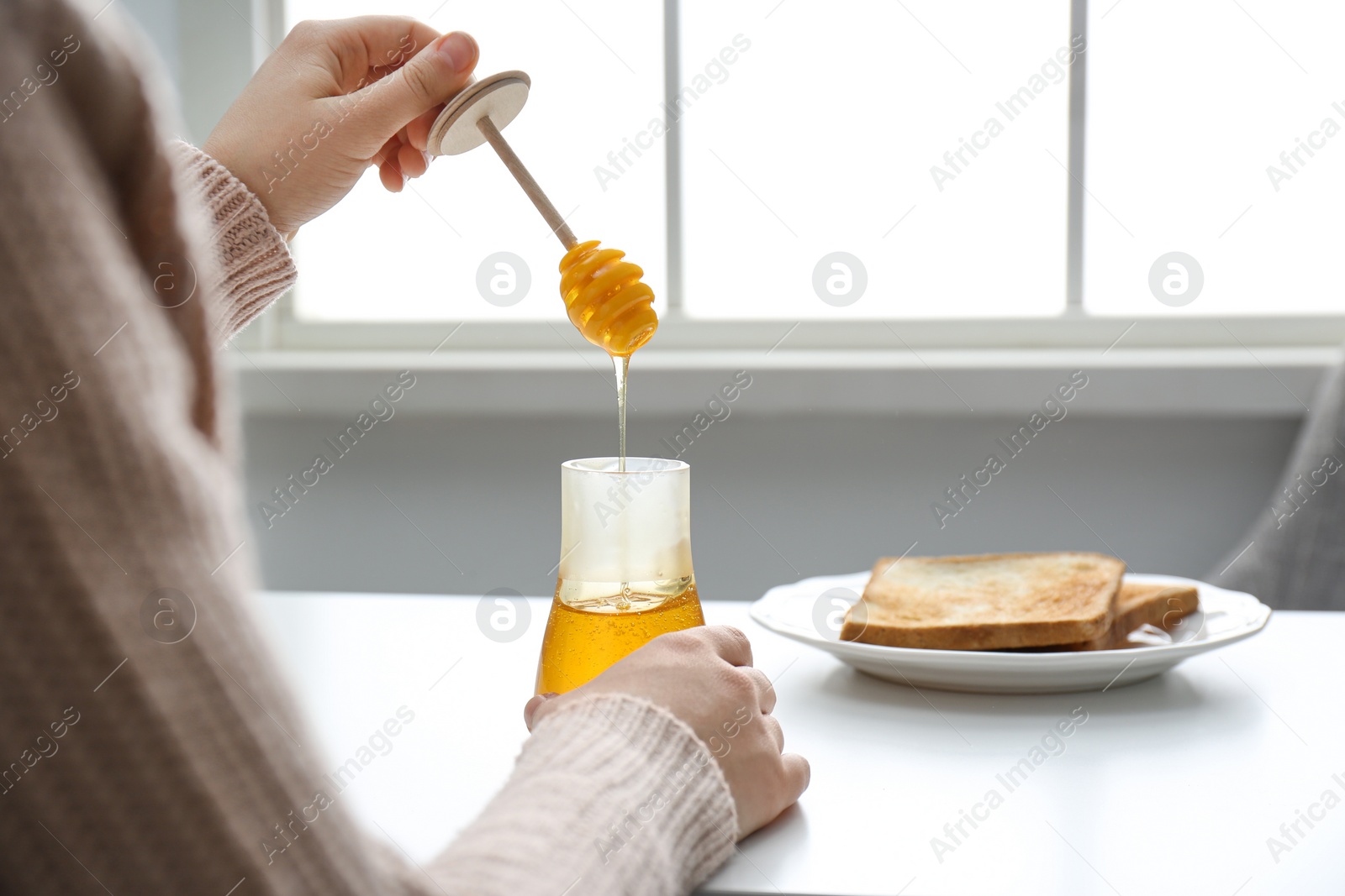 Photo of Woman with honey and dipper at white table, closeup