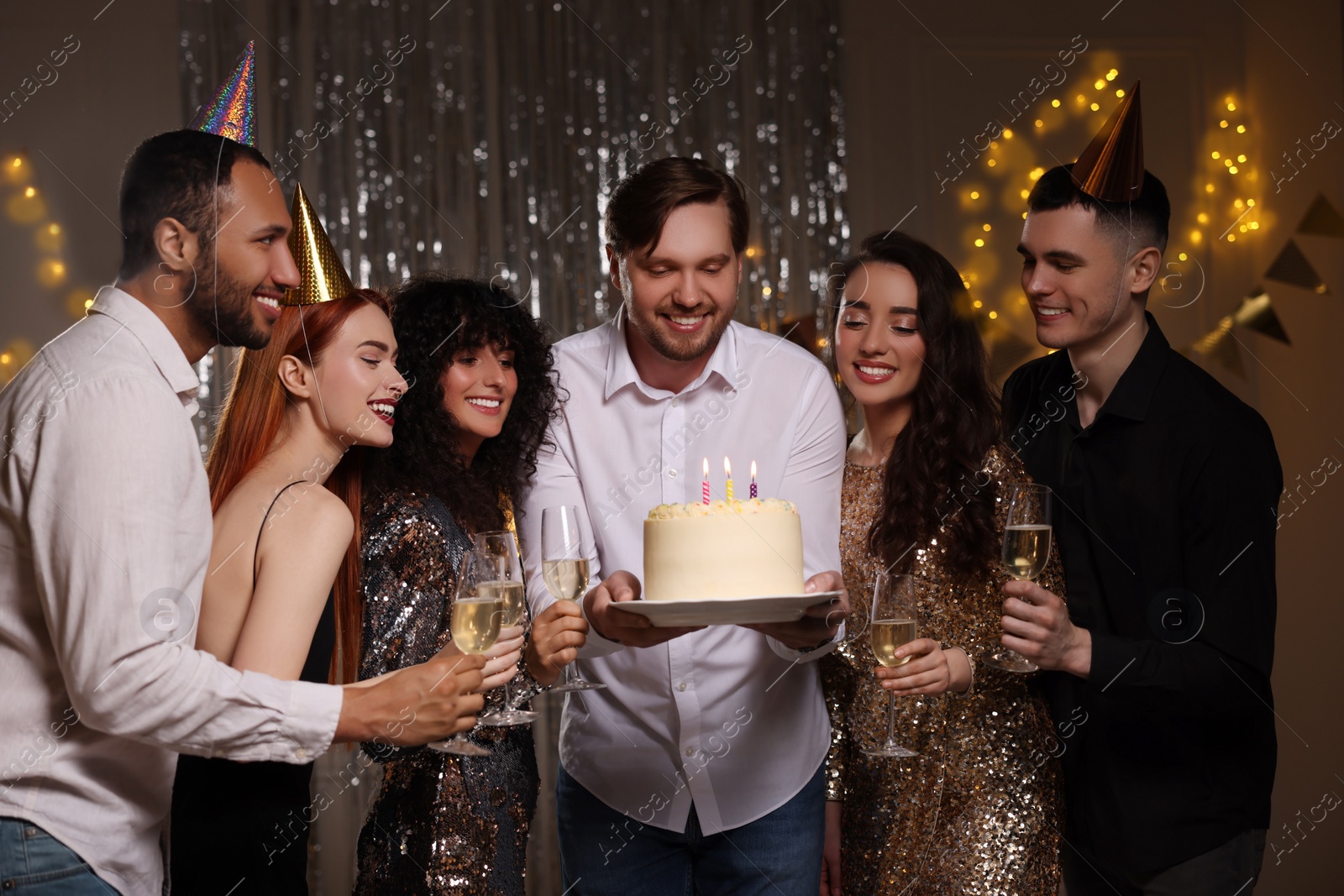 Photo of Happy friends with tasty cake and glasses of sparkling wine celebrating birthday indoors