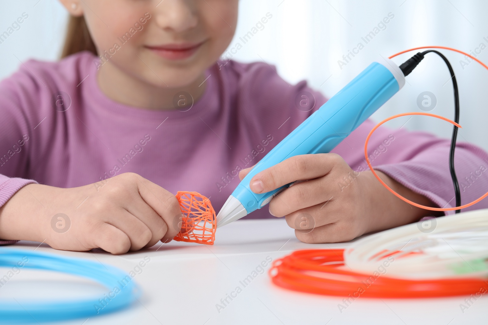 Photo of Girl drawing with stylish 3D pen at white table indoors, closeup