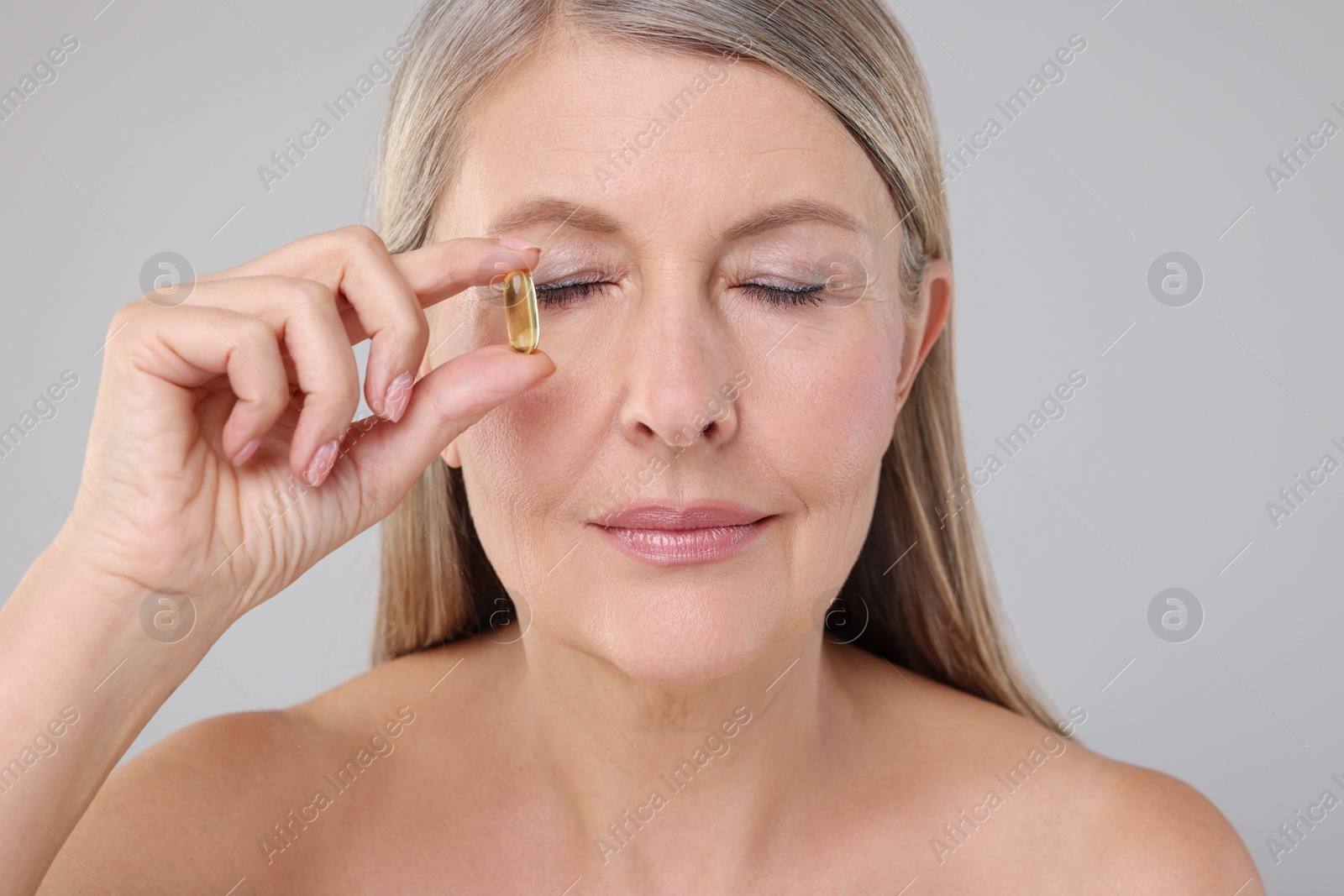 Photo of Beautiful woman with vitamin capsule on grey background