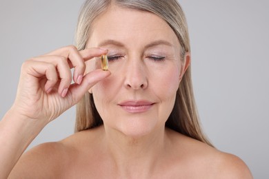 Beautiful woman with vitamin capsule on grey background