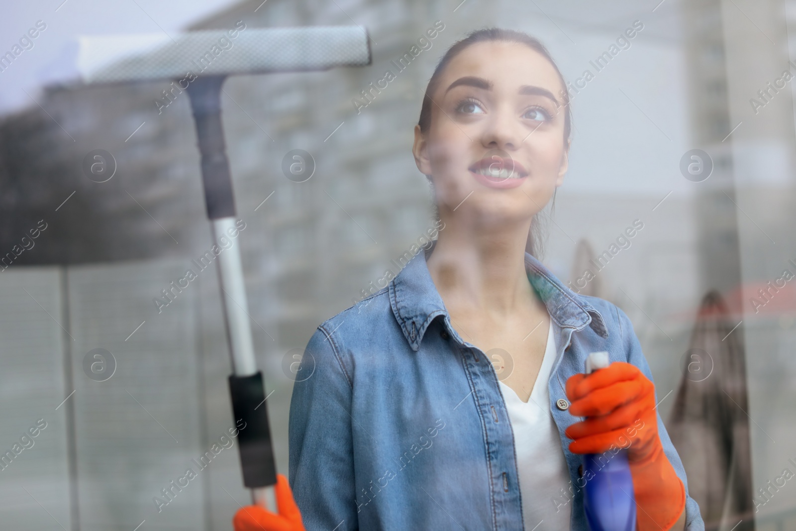 Photo of Young woman cleaning window glass at home