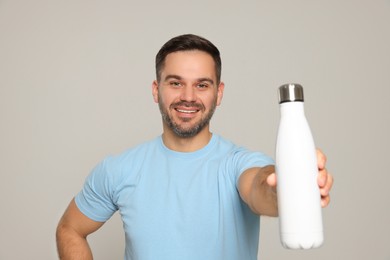 Happy man showing thermo bottle on light grey background
