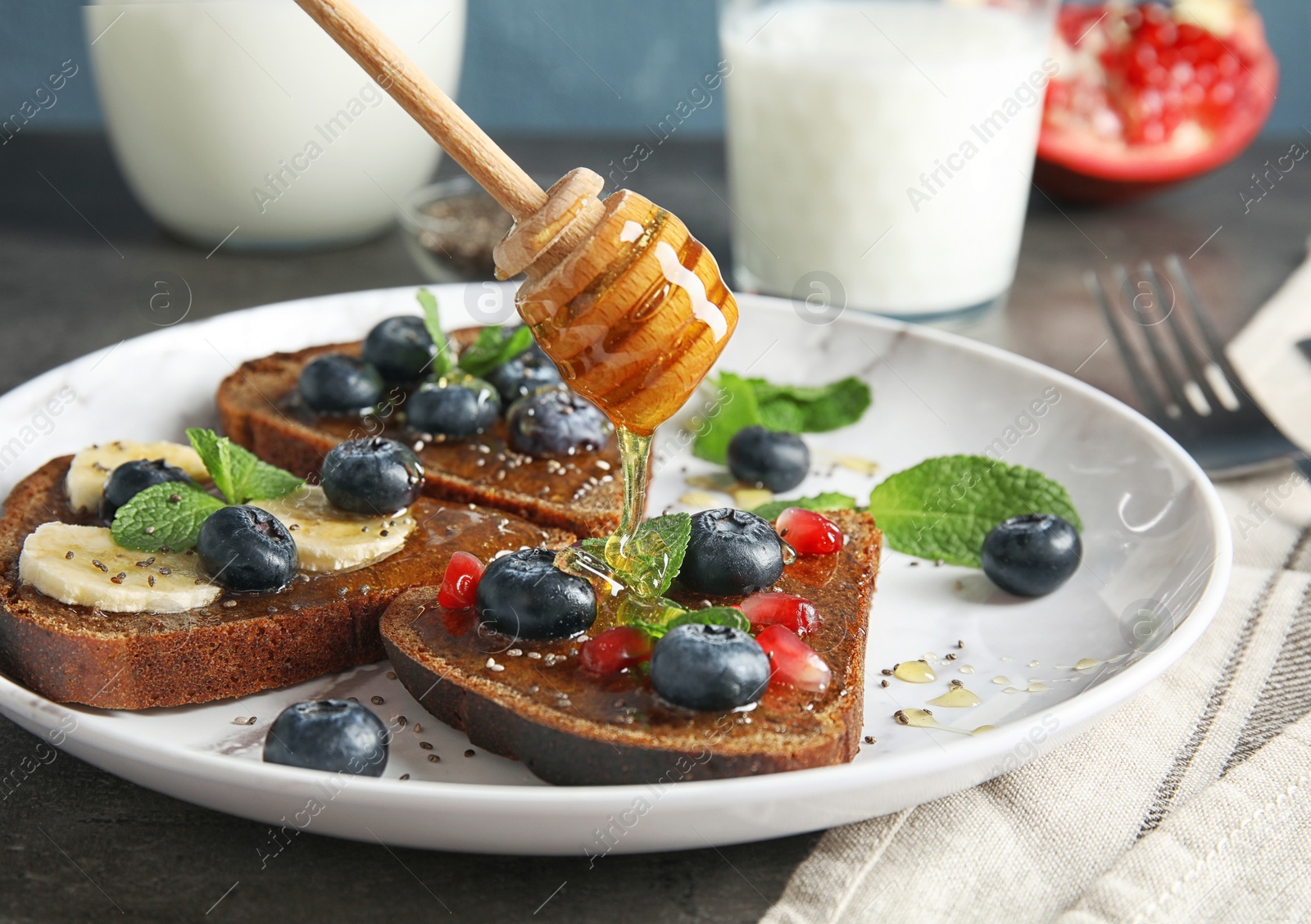 Photo of Pouring honey onto toasts with blueberries and chia seeds on plate
