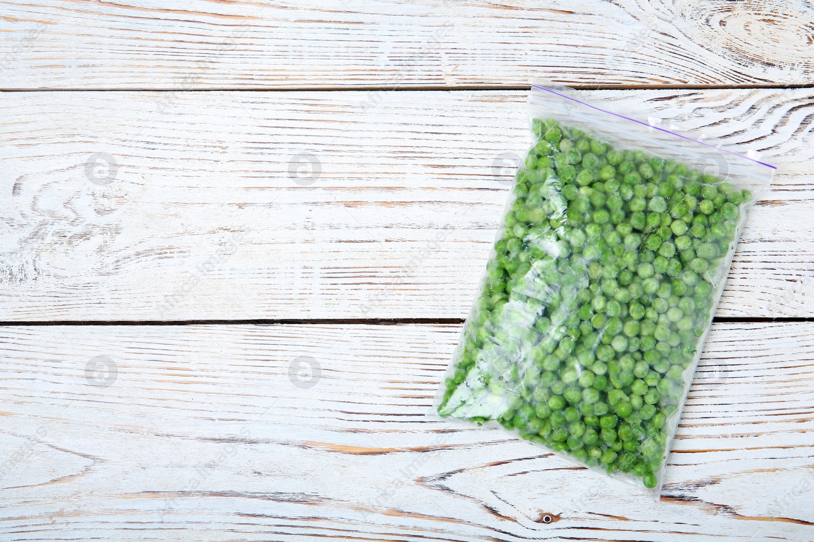 Photo of Plastic bag with frozen peas on wooden background, top view. Vegetable preservation