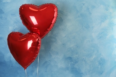 Photo of Red heart shaped balloons near light blue wall, space for text. Valentine's Day celebration