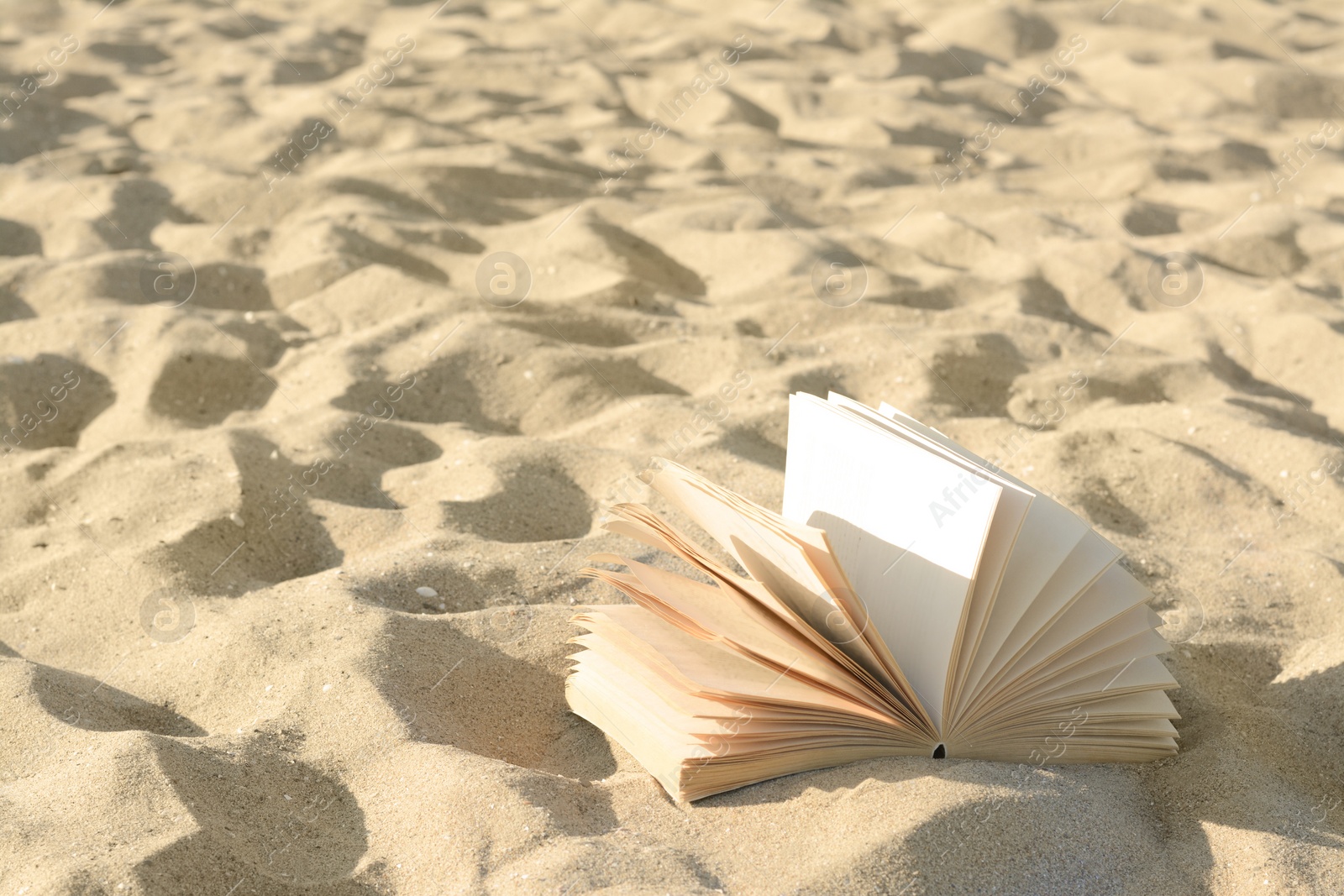 Photo of Open book on sandy beach. Space for text