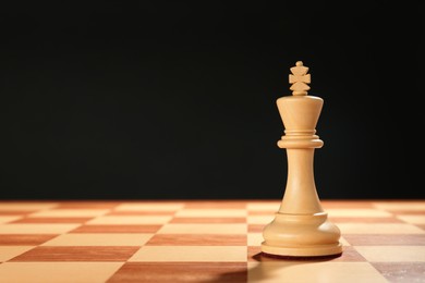 Photo of Wooden king on chessboard against dark background, space for text