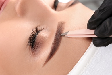 Photo of Young woman having professional eyebrow correction procedure in beauty salon