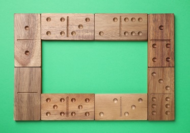 Frame made of wooden domino tiles on green background, flat lay. Space for text