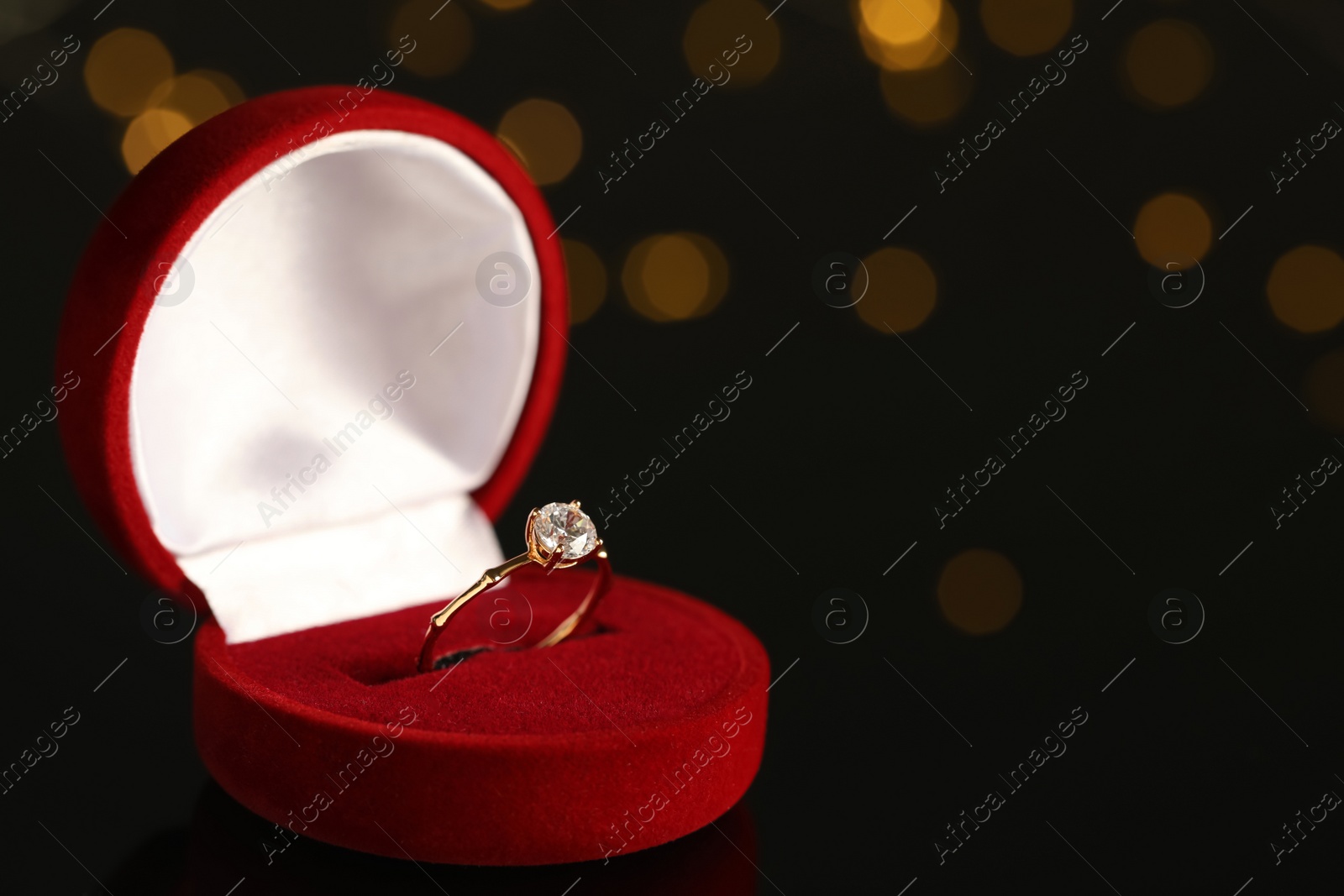 Photo of Beautiful engagement ring in red box against blurred festive lights, space for text