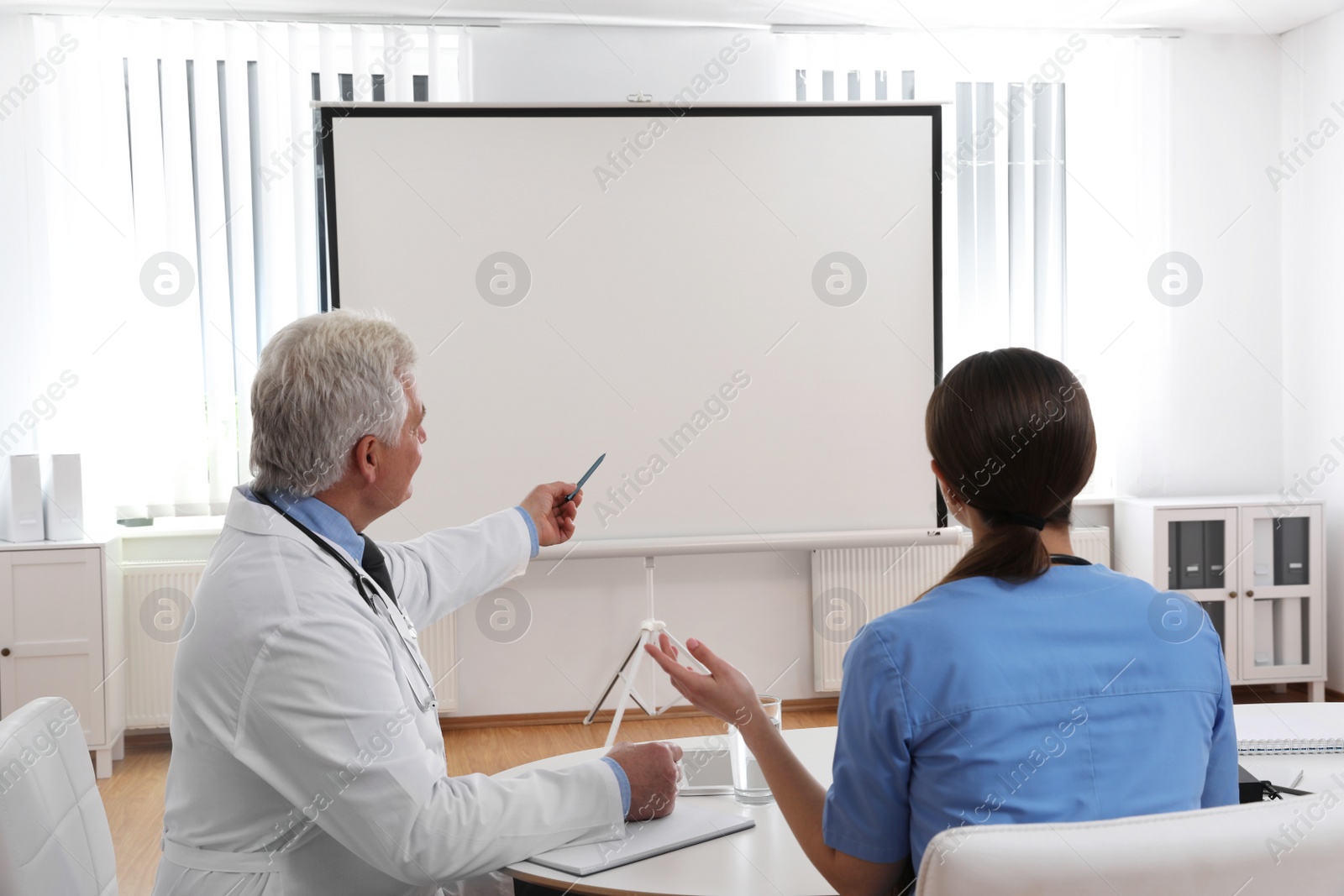 Photo of Team of doctors looking at projection screen indoors. 
Video conference