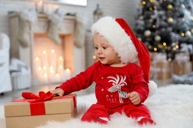 Photo of Little baby with Santa hat and Christmas gift on floor at home