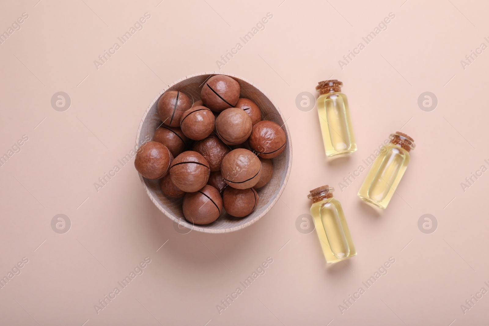 Photo of Delicious organic Macadamia nuts and cosmetic oil on beige background, flat lay