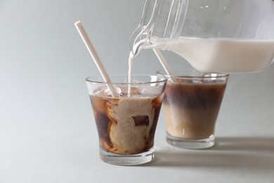 Photo of Pouring milk into glass with refreshing iced coffee on grey background, closeup. Space for text