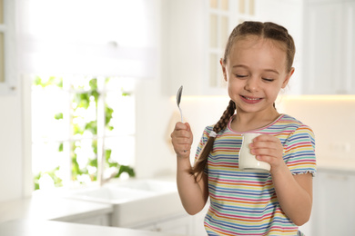 Photo of Cute little girl with tasty yogurt in kitchen. Space for text