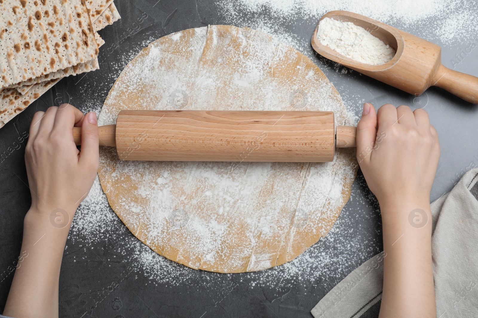 Photo of Woman rolling raw dough for traditional matzo at grey table, top view
