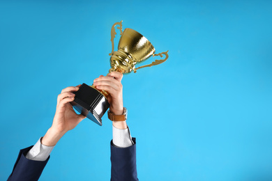 Photo of Businessman holding gold trophy cup on light blue background, closeup. Space for text
