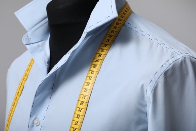 Photo of Semi-ready shirt with tailor's measuring tape on mannequin against grey background, closeup