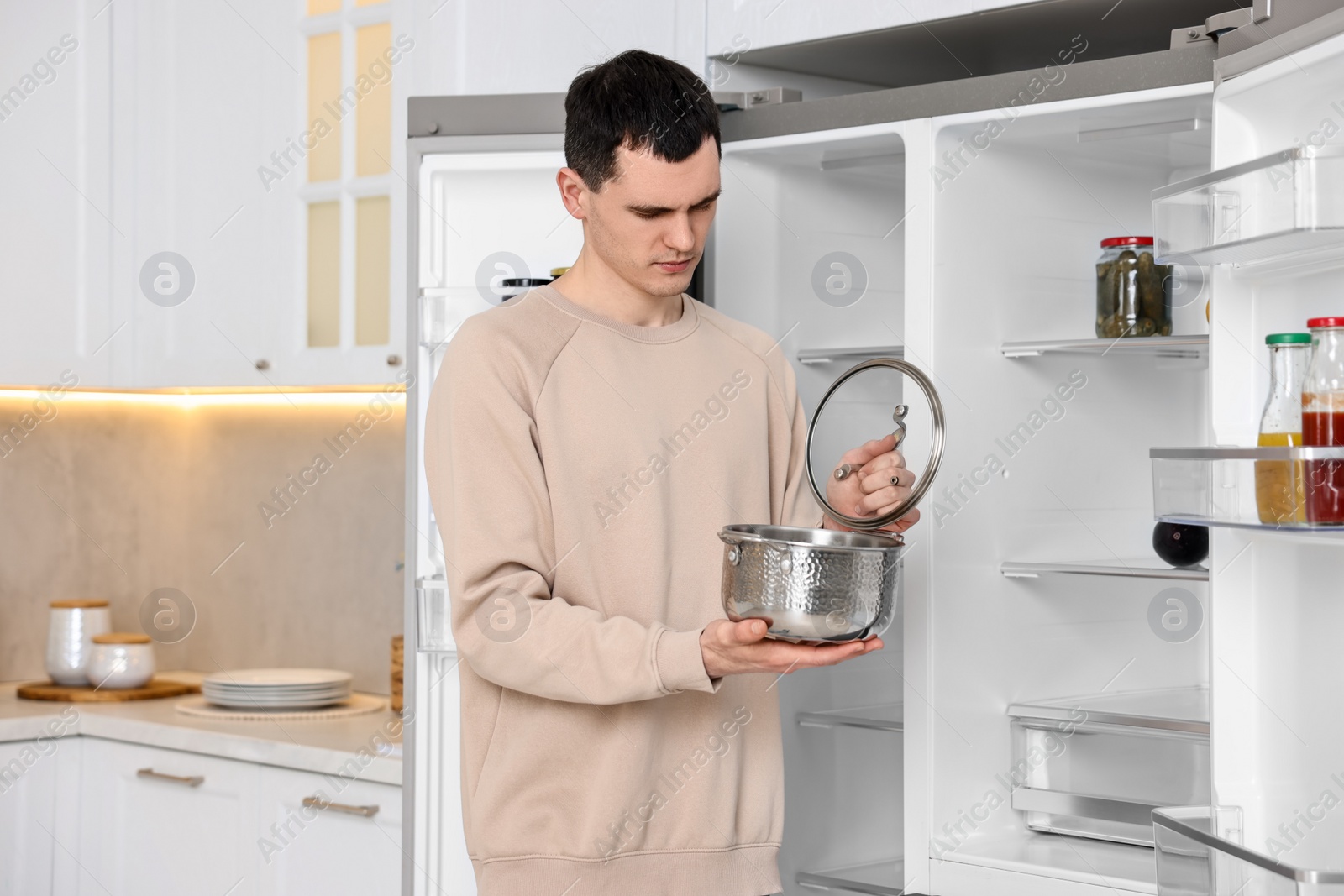 Photo of Upset man with pot near empty refrigerator in kitchen