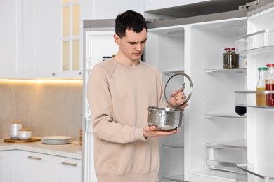 Upset man with pot near empty refrigerator in kitchen